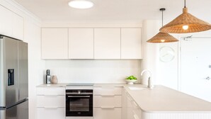 Une cuisine moderne avec des meubles blancs, un four encastré, un réfrigérateur en acier inoxydable et un grand îlot central doté d’un évier.