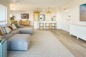 A modern living room with a sectional sofa, a dining area, and a kitchen with bar stools.
