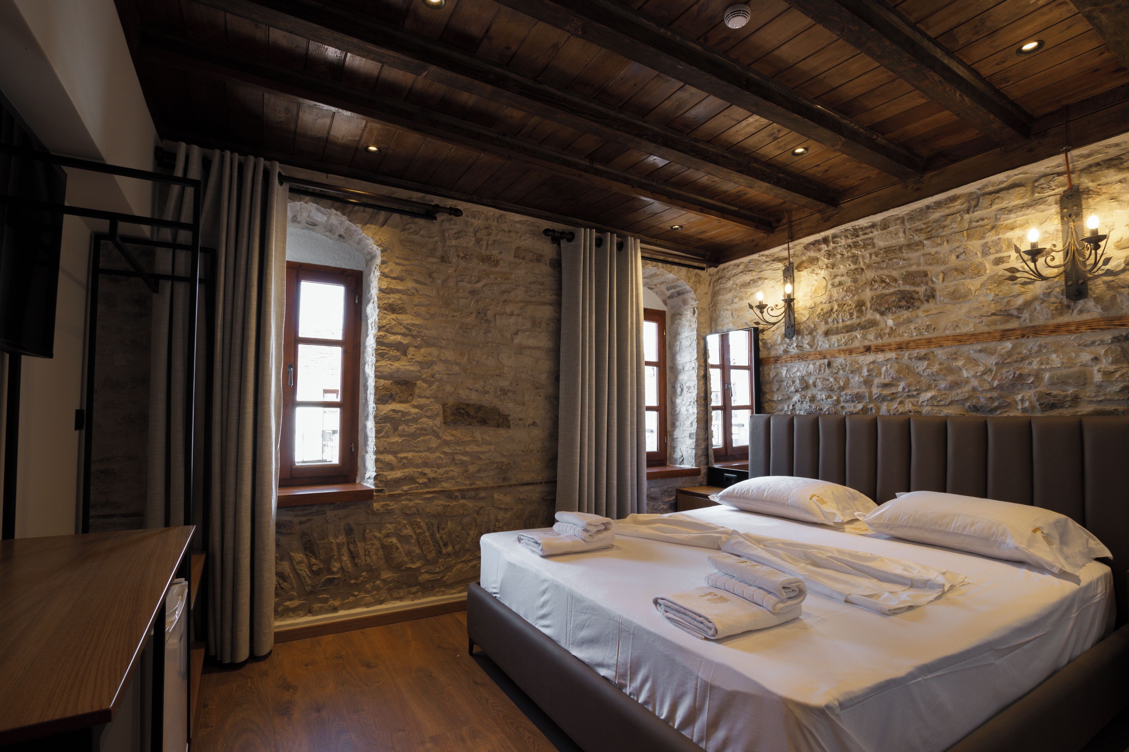 Een slaapkamer met stenen wanden, een houten plafond en een bed met keurig opgevouwen handdoeken.