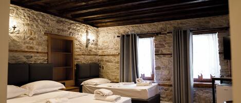A room with two beds, stone walls, wooden beams, a desk, and a window with curtains.