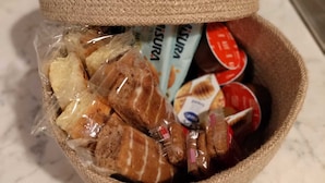 Een gevlochten mand met verschillende etenswaren, waaronder brood en verpakte producten, op een marmeren aanrecht.