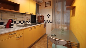 Een compacte keuken met gele kastjes, een spoelbak, een fornuis en een eethoek met een glazen tafel en stoelen.