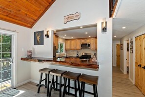 A modern kitchen with a bar area, wooden cabinets, and a ceiling with exposed beams.