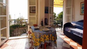 An open-plan living and dining area with a balcony, a dining table set with plates and glasses, and a sofa. - Appartamenti Giada Studio Apartment 4 Pax Casa Giada (Moneglia)