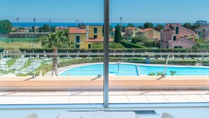 A dining table with white chairs and a rose centerpiece, overlooking a pool and coastal houses. - Residence Loano 2 Village Two-room Apartment 4 Pax Balcony (Loano)