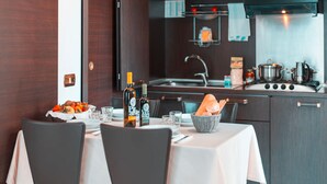 A modern kitchen with dark cabinetry, a stainless steel stove, and a sink. There is a dining table with chairs, a bottle of wine, and a basket of bread. - Residence Loano 2 Village Two-room Apartment 4 Pax Balcony (Loano)