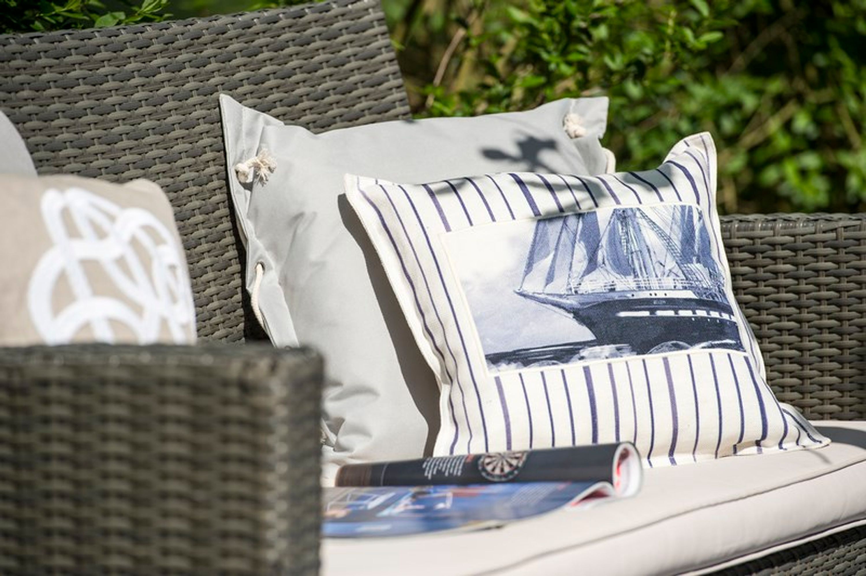 A wicker sofa with two pillows, one plain and one with a striped design.