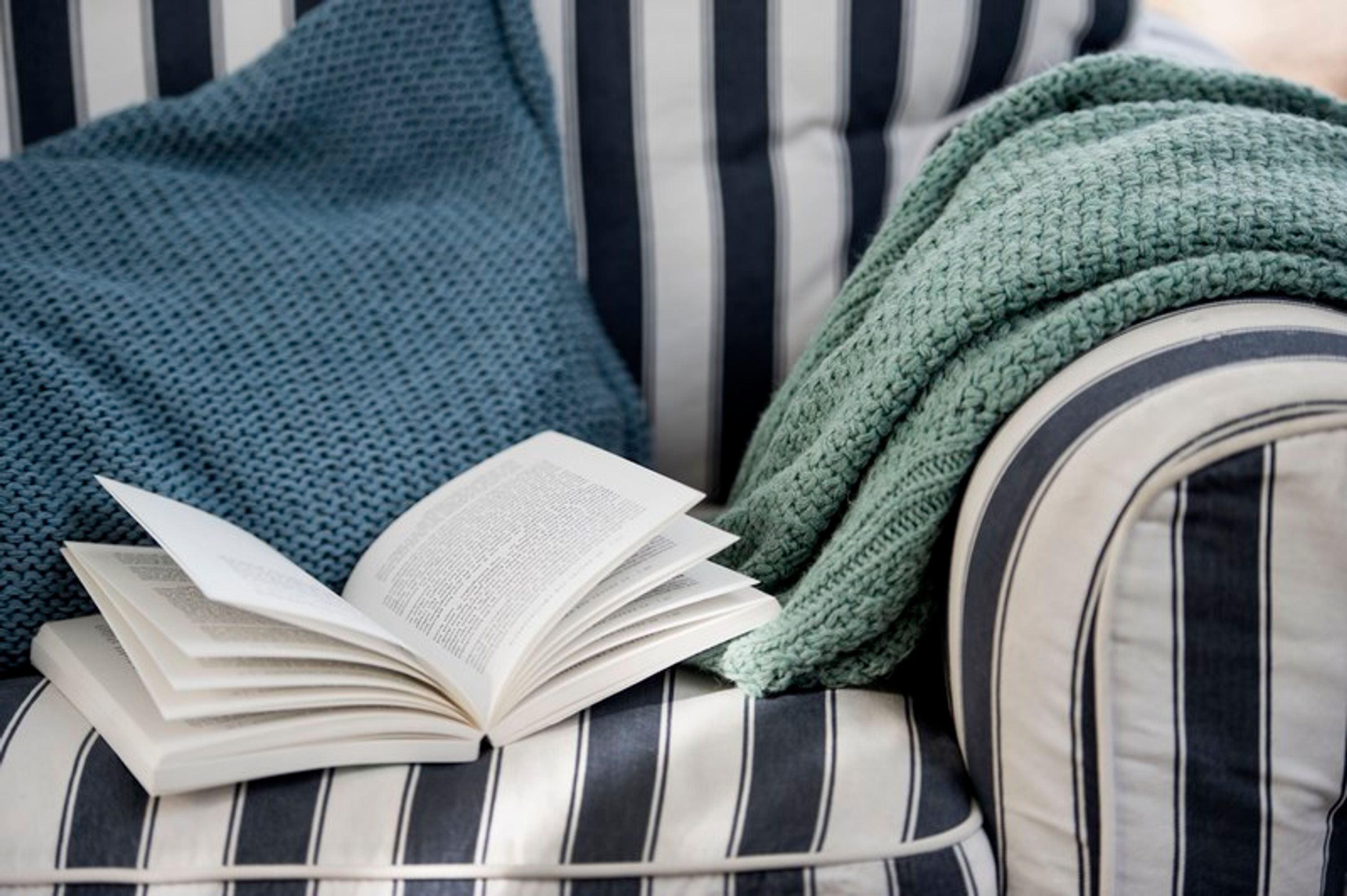 Un canapé à rayures, avec un livre et une couverture verte en tricot.