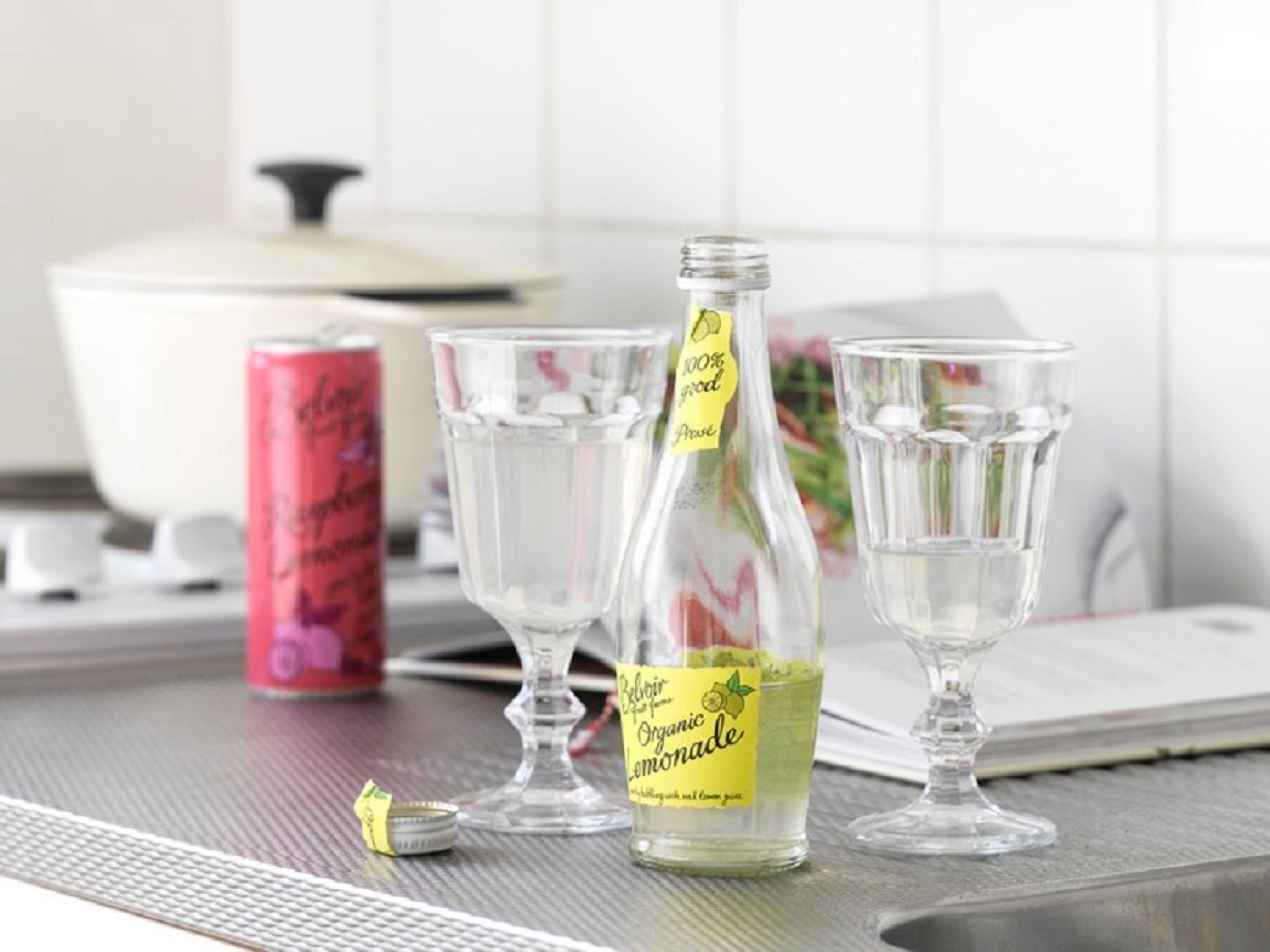 Una encimera de cocina con una botella de limonada orgánica, dos vasos y una lata de refresco.