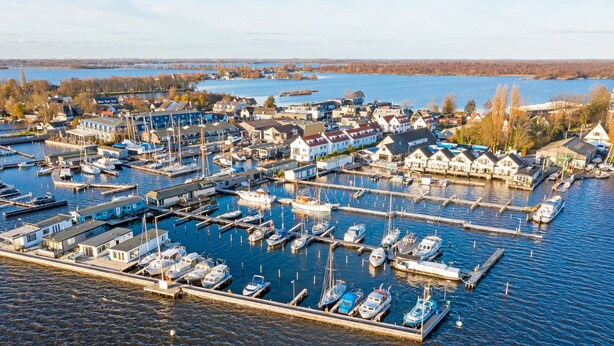 A marina with numerous boats docked, surrounded by residential buildings and a body of water in the background. - Penthouse in Loosdrecht (Loosdrecht)