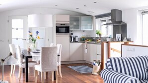 A modern kitchen with white cabinets, a microwave, and a stove. There is a dining area with a table and chairs, and a striped sofa in the living area. - Watervilla in Loosdrecht (Loosdrecht)