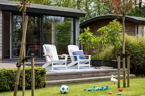 A modern house with a deck, two white lounge chairs, and a duck walking nearby. - Watervilla in Loosdrecht (Loosdrecht)