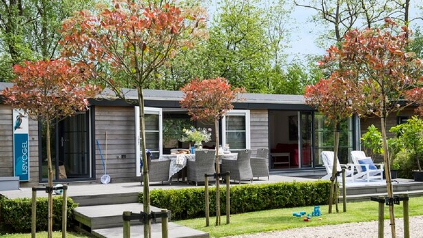 A modern outdoor seating area with a table and chairs, a covered patio, and a well-maintained garden with trees and hedges. - Watervilla in Loosdrecht (Loosdrecht)