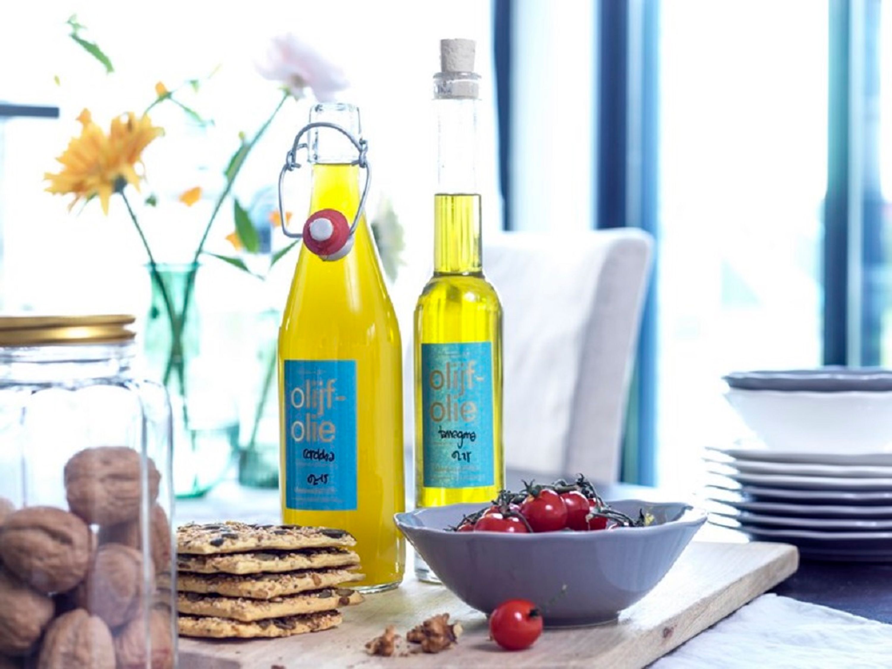 A breakfast setting with two bottles of olive oil, a bowl of cherries, and a stack of cookies on a wooden board.