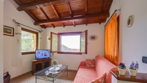 Una sala de estar acogedora con techo de madera, un sofá, una mesa de centro de vidrio y una televisión.