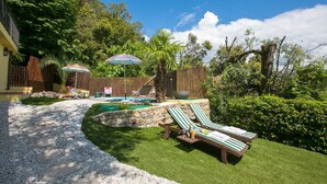 Un patio trasero con piscina, dos sillas de descanso y una palmera.