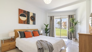A modern bedroom with a large bed, a nightstand, a wooden dresser, and a view of the outside. - Waterside marina view 3 bedroom apartment with private pool in Puerto Sotogrande (San Roque)