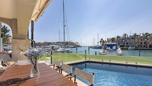 A poolside area with a wooden table, chairs, and a vase of flowers. - Waterside marina view 3 bedroom apartment with private pool in Puerto Sotogrande (San Roque)