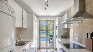 A modern kitchen with white cabinetry, a built-in oven, and a large window overlooking a pool. - Waterside marina view 3 bedroom apartment with private pool in Puerto Sotogrande (San Roque)