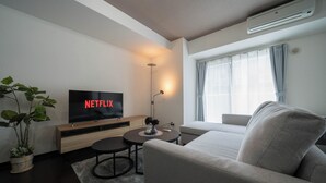 Un soggiorno moderno con una TV a schermo piatto che mostra 'NETFLIX', un divano, un piccolo tavolino con una lampada e una pianta in vaso.