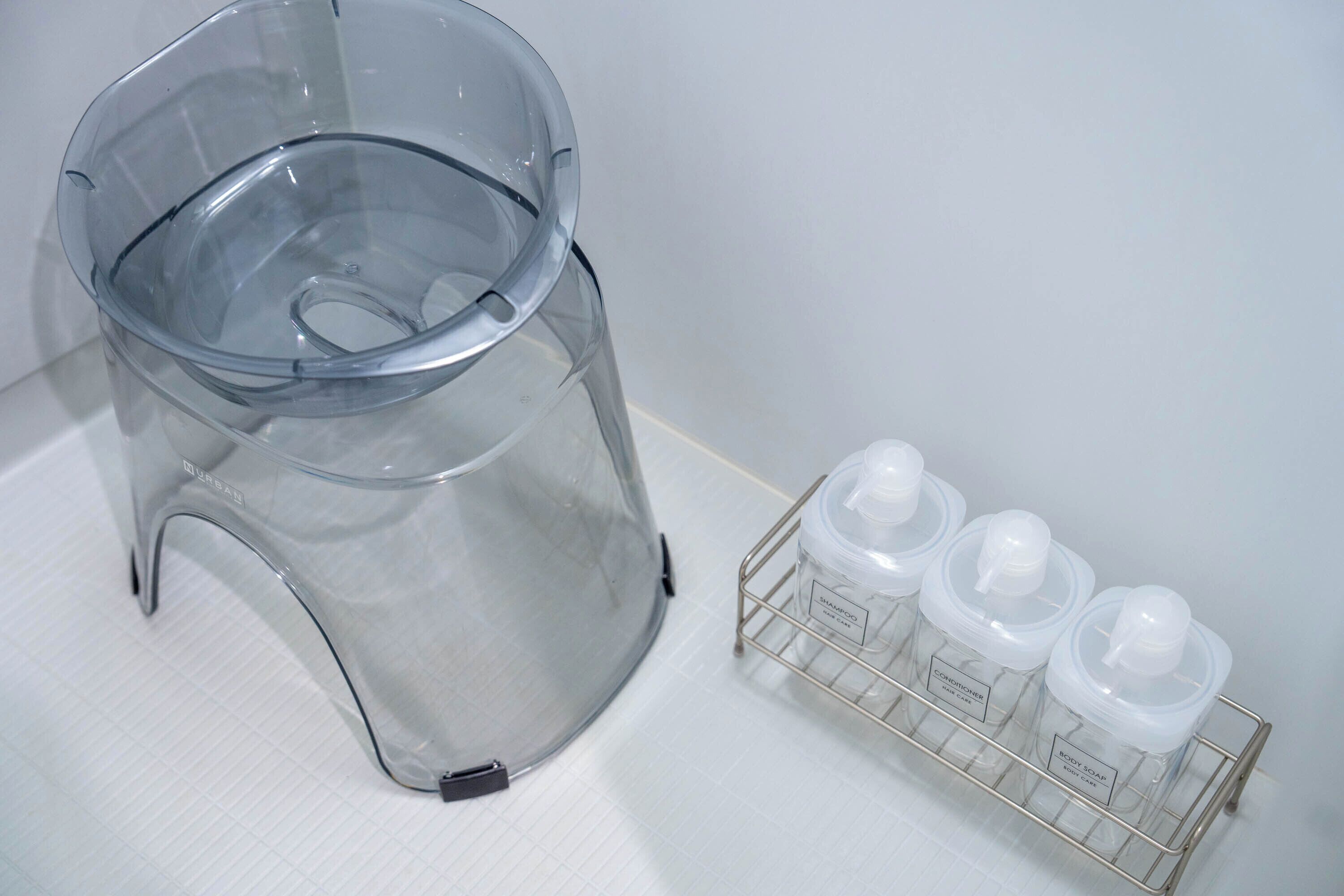 Un dispensador de filtro de agua transparente y un estante metálico con tres botellas de champú.