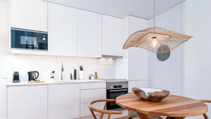 A modern kitchen with white cabinetry, a built-in microwave, and a round wooden dining table with woven chairs. - Limehome Evora Rua de Machede 52 (Évora)