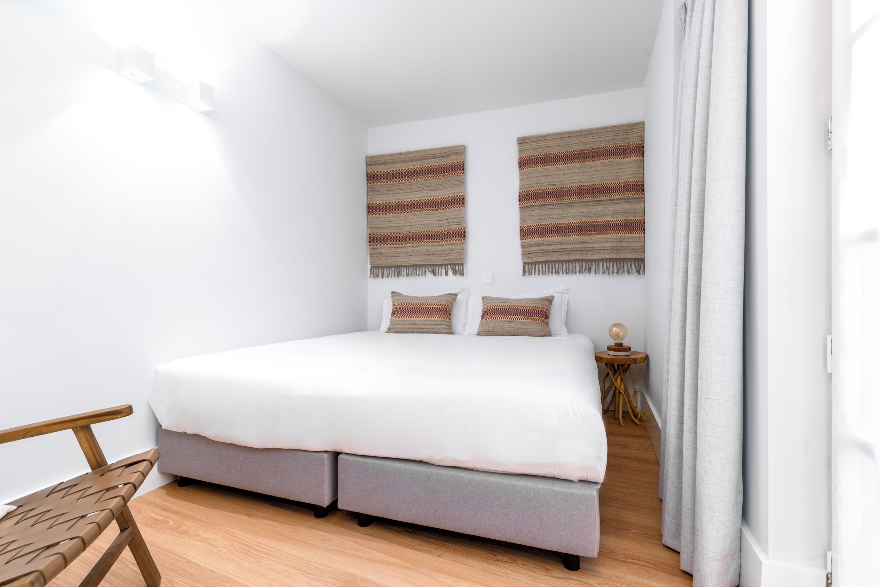 Un dormitorio moderno con cama, un banco de madera y dos elementos decorativos en la pared.