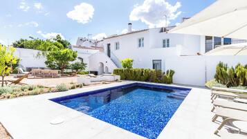 Relax by the rectangular pool surrounded by a white building and lush greenery.
