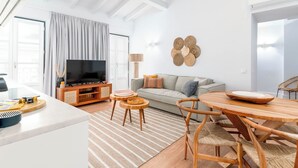 A modern living room with a TV, sofa, and dining area. - Limehome Evora Rua de Machede 52 (Évora)