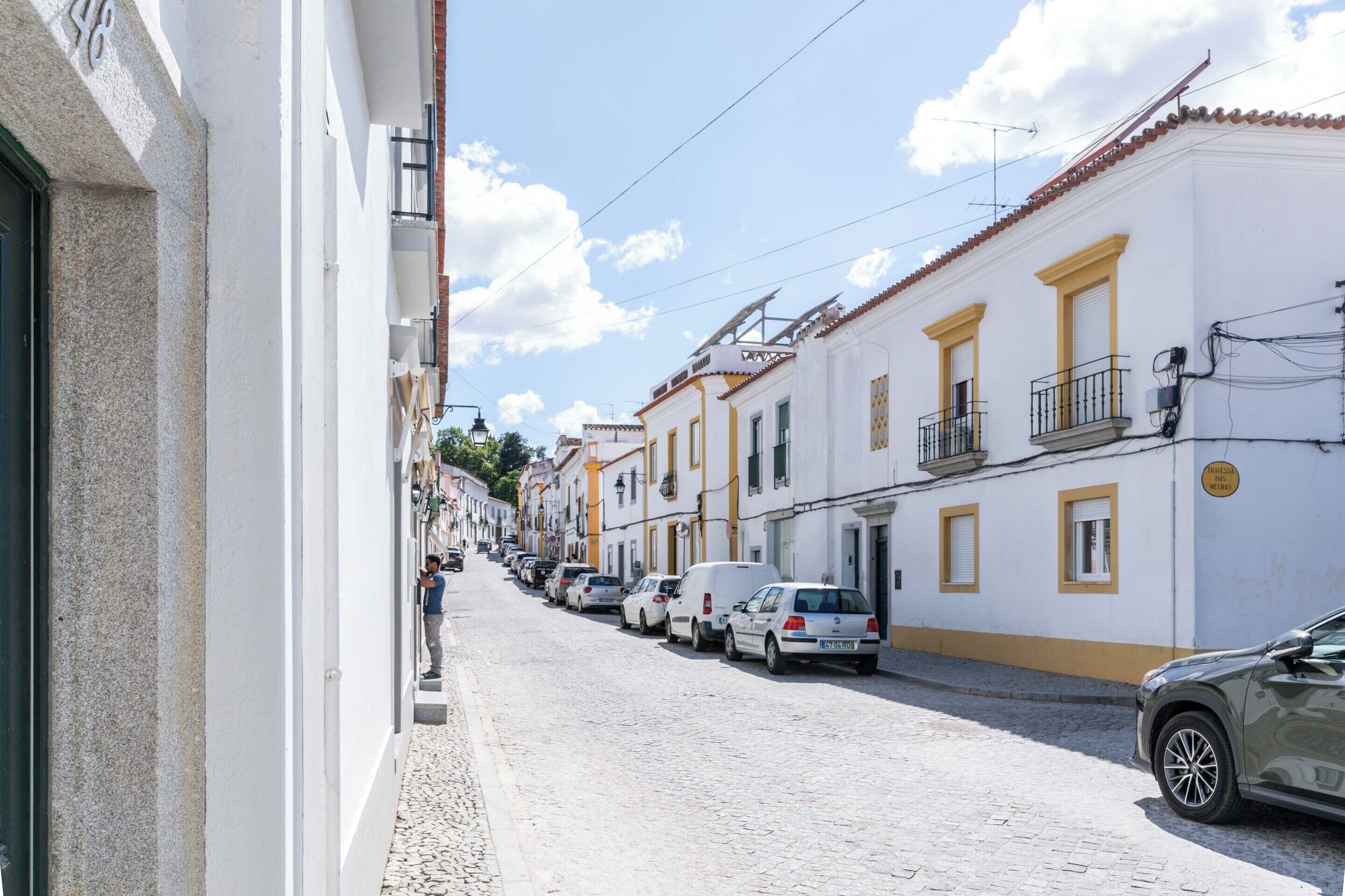 A narrow cobblestone street lined with white buildings with yellow trim and balconies.
