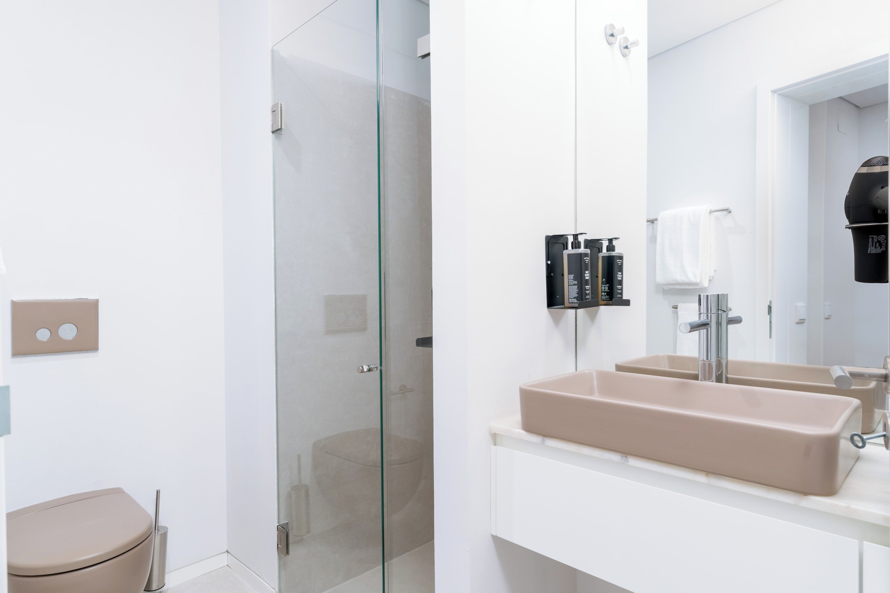 Un baño moderno con cabina de ducha de vidrio, un lavabo color crema y un mueble de tocador blanco.