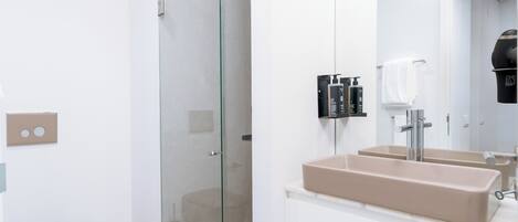 Un baño moderno con cabina de ducha de vidrio, un lavabo color crema y un mueble de tocador blanco.