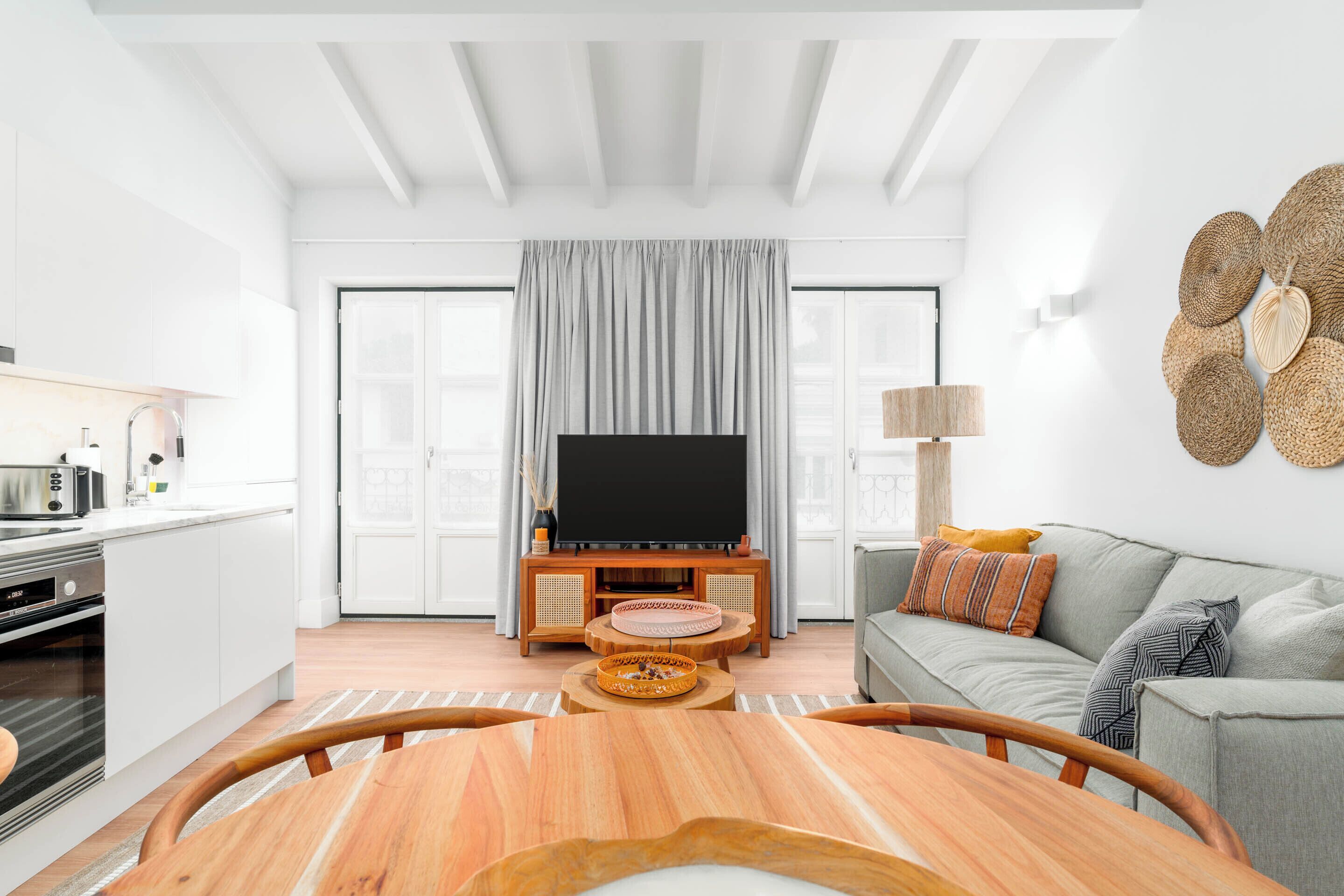 Una sala de estar moderna con un televisor de pantalla plana, cortinas grises, un sofá gris y una mesa de centro de madera.