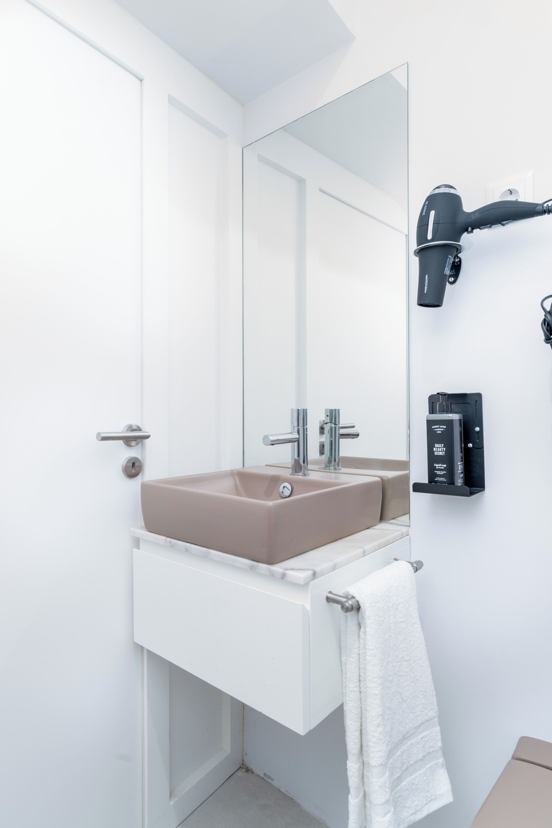 A modern bathroom with a beige sink, a white towel rack, and a hair dryer mounted on the wall.