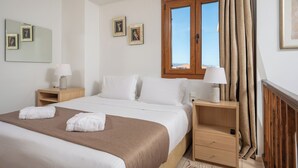 Een hotelkamer met een groot bed, twee nachtkastjes, een raam met gordijnen en ingelijste foto’s aan de muur.