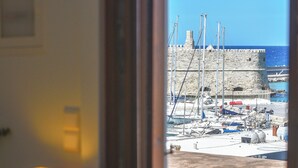 Uitzicht vanuit een kamer met een raam op een haven, met boten en een historisch stenen gebouw.
