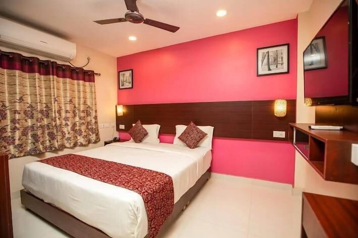 A hotel room with a bed, a ceiling fan, a red wall, and a wooden headboard.