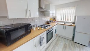 A modern kitchen with white cabinets, a microwave, a gas stove, a washing machine, and a refrigerator. - Book Direct 10% Off > Flexley House 4 Br Workstays (Middlesbrough)