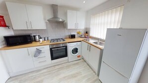 A modern kitchen with white cabinets, a stainless steel range hood, a built-in oven, a washing machine, and a grey refrigerator. - Book Direct 10% Off > Flexley House 4 Br Workstays (Middlesbrough)