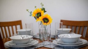 Et spisebord dækket med hvide tallerkener, skåle og klare glas, med en vase med solsikker i midten.