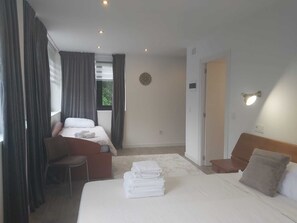 A hotel room with a bed, a chair, a desk, and a window with curtains.