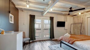 Ein Schlafzimmer mit einem Bett, einem Schreibtisch, einem Sessel, einem Fernseher und einem Deckenventilator.