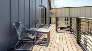 Eine Holzterrasse mit Metallstühlen und einem Tisch, angrenzend an ein Gebäude mit senkrechten Holzverkleidungen.