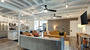 Eine moderne Küche mit Edelstahlgeräten, ein Essbereich mit einem Holztisch und ein Wohnbereich mit einer Couch und Sesseln.