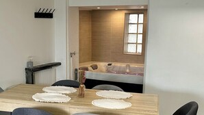 A modern dining area with a wooden table, grey upholstered chairs, and a view of a spa room with a bathtub and a window. - 2 Bedroom Private vacation home in Amboise (Amboise)