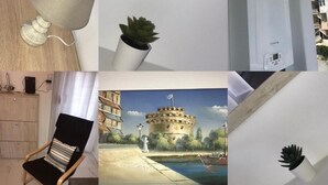 A room with a lamp, a potted plant, a heater, a chair, a painting of a castle, a coffee maker, and a shelf with decorative items. - Cozy Apartment With two Bedrooms With a sea View (Thermaikos)