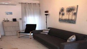 A living room with a dark grey sofa, a black chair, a wooden cabinet, and a painting of trees on the wall. - Cozy Apartment With two Bedrooms With a sea View (Thermaikos)