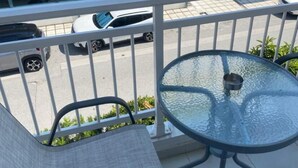 A balcony with a glass table and chairs, overlooking a parking area with cars and a building with a sign reading "Fit & Fight". - Cozy Apartment With two Bedrooms With a sea View (Thermaikos)