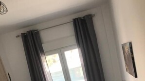 A bedroom with a bed, a window with curtains, a radiator, and a small table with a lamp. - Cozy Apartment With two Bedrooms With a sea View (Thermaikos)