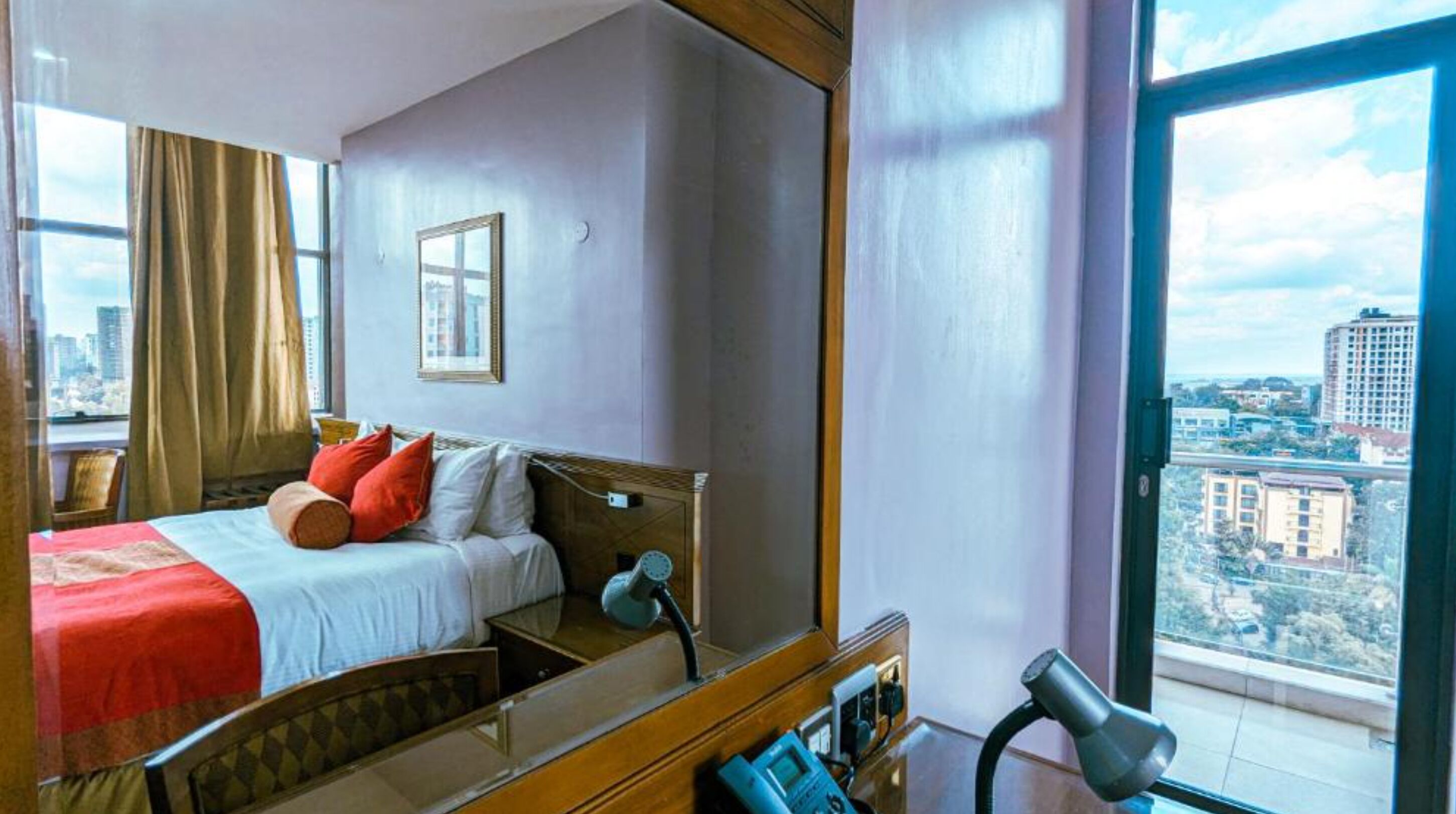 Een hotelkamer met een bed, een grote spiegel, een haardroger en uitzicht op de stad door het raam.